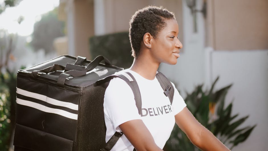 A woman with short curly hair, wearing a white T-shirt with the word 'DELIVER' and a black backpack, is depicted in profile walking outdoors. She has a focused expression and is standing in front of a