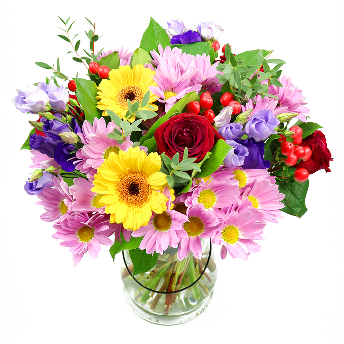A lush, dome-shaped bouquet bursts from a cylindrical glass vase, its many flowers arranged in a rich tapestry of colour and texture against a neutral white backdrop. In the centre, deep red roses anchor the composition, their velvety petals spiralling inward to form classic, full blooms that feel both passionate and reassuringly familiar. Beside them, bright yellow gerbera daisies with dark, coffee-toned centres stand tall, their bold, open faces radiating the same kind of energy you might feel walking through Homerton's lively weekend markets. Around this central cluster, numerous pink and lilac chrysanthemums spread out in generous sprays, each blossom made up of slender petals that create a soft, cushiony effect, adding volume and a delicate, almost feathery texture. Woven among these are elegant lisianthus flowers in shades of rich purple and cool lavender; some blossoms are fully open and cup-shaped, others still partially closed, lending a sense of movement and unfolding life. Small clusters of round, glossy red hypericum berries nestle between petals and leaves, introducing a playful, bead-like texture that contrasts with the softness of the blooms. A mix of greenery supports and frames the flowers: smooth, broad leaves give the arrangement structure, while lighter, more elongated stems arc gently outward, keeping the bouquet from feeling too dense. Through the transparent sides of the vase, you can see a tidy fan of green stems submerged in crystal-clear water, hinting at professional care and freshness. The lighting is soft and even, without dramatic shadows, so every hue-from crimson and sunshine yellow to blush pink and royal purple-appears distinct yet harmonious. The bouquet's overall mood is joyful and generous, perfectly suited for celebrating birthdays, new homes, or simple everyday victories with a delivery to friends, family, or colleagues around Homerton.